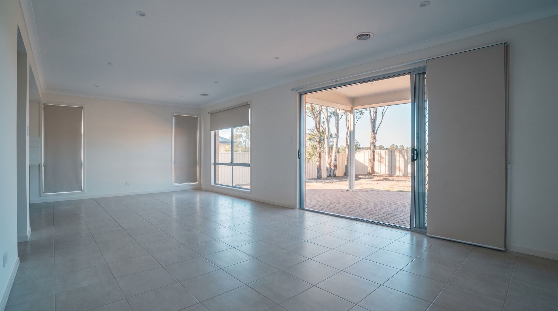 An empty open-plan living and dining area with tiled floors and doors open to a paved courtyard