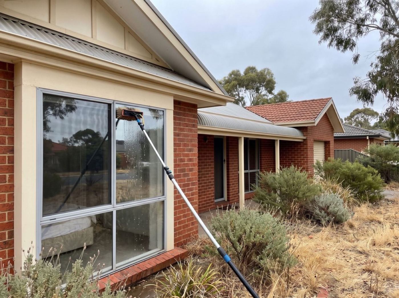 A window on a brick home being washed with a pole and brush
