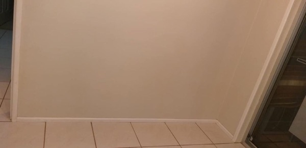 A tiled bathroom floor and painted wall meeting at the skirting