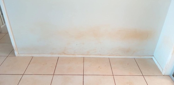 The same tiled floor and wall with brown staining across the lower wall