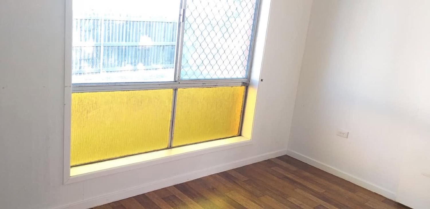 An empty room with a window, timber floor and plain painted walls after a vacate clean