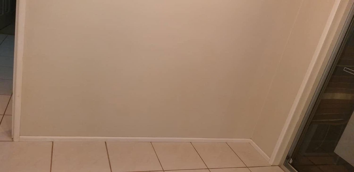A tiled bathroom floor and painted wall meeting at the skirting